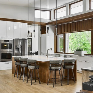 Esempio di una grande cucina design con ante lisce, ante bianche, top in quarzo composito, elettrodomestici in acciaio inossidabile, parquet chiaro, isola, pavimento beige, lavello stile country, paraspruzzi a finestra e top bianco