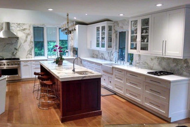 Eat-in kitchen - mid-sized transitional l-shaped medium tone wood floor eat-in kitchen idea in New York with a farmhouse sink, shaker cabinets, white cabinets, marble countertops, multicolored backsplash, stone slab backsplash, stainless steel appliances and an island