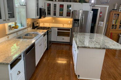 Inspiration for a mid-sized contemporary medium tone wood floor and brown floor eat-in kitchen remodel in Birmingham with an undermount sink, shaker cabinets, white cabinets, granite countertops, white backsplash, subway tile backsplash, stainless steel appliances, an island and white countertops