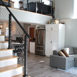 Inspiration for a mid-sized beach style l-shaped eat-in kitchen in Detroit with a farmhouse sink, shaker cabinets, white cabinets, granite benchtops, white splashback, ceramic splashback, stainless steel appliances, vinyl floors, with island, grey floor and black benchtop.