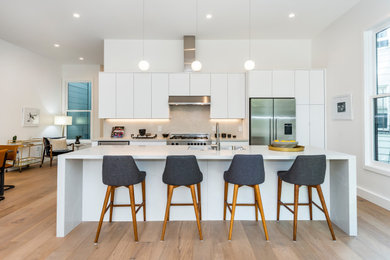 This is an example of a medium sized contemporary galley open plan kitchen in San Francisco with a submerged sink, flat-panel cabinets, white cabinets, engineered stone countertops, white splashback, engineered quartz splashback, stainless steel appliances, light hardwood flooring, an island, beige floors and white worktops.