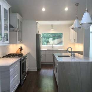 Contemporary open concept kitchen designs - Trendy l-shaped brown floor open concept kitchen photo in Atlanta with glass-front cabinets, an island, an undermount sink, white cabinets, quartzite countertops, white backsplash, subway tile backsplash and stainless steel appliances