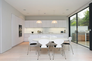 Идея дизайна: кухня-гостиная в современном стиле с плоскими фасадами, белыми фасадами, столешницей из акрилового камня, островом и светлым паркетным полом