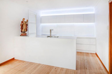Foto de cocina lineal contemporánea de tamaño medio abierta con fregadero integrado, puertas de armario amarillas, salpicadero blanco, electrodomésticos blancos, suelo de madera clara y una isla