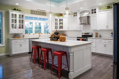 Example of a large country u-shaped medium tone wood floor and brown floor eat-in kitchen design in Other with a farmhouse sink, shaker cabinets, white cabinets, quartzite countertops, white backsplash, subway tile backsplash, stainless steel appliances, an island and white countertops