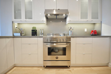 Idee per una cucina a L design di medie dimensioni con ante lisce, ante bianche, paraspruzzi grigio, elettrodomestici in acciaio inossidabile, pavimento in compensato e pavimento marrone