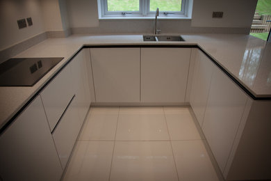 This is an example of a medium sized contemporary u-shaped kitchen/diner in West Midlands with flat-panel cabinets, white cabinets, quartz worktops and no island.
