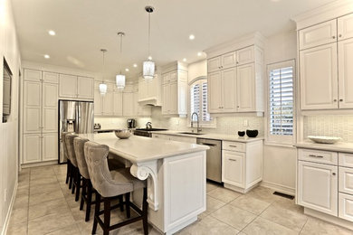 Eat-in kitchen - l-shaped porcelain tile eat-in kitchen idea in Toronto with an undermount sink, raised-panel cabinets, white cabinets, quartz countertops, white backsplash, glass tile backsplash, stainless steel appliances and an island