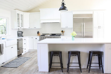 Example of a large farmhouse l-shaped vinyl floor open concept kitchen design in Seattle with a farmhouse sink, shaker cabinets, white cabinets, quartz countertops, white backsplash, subway tile backsplash, stainless steel appliances and an island