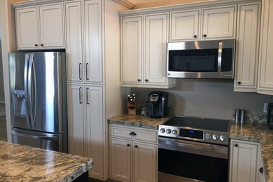 Photo of a medium sized classic l-shaped kitchen/diner in Phoenix with a double-bowl sink, recessed-panel cabinets, white cabinets, grey splashback, stainless steel appliances and an island.
