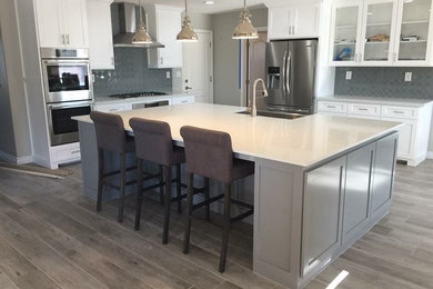 Eat-in kitchen - large transitional u-shaped laminate floor and gray floor eat-in kitchen idea in Los Angeles with shaker cabinets, white cabinets, quartzite countertops, gray backsplash, ceramic backsplash, stainless steel appliances, an island and white countertops