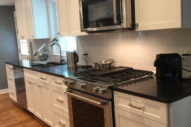 Example of a mid-sized transitional galley light wood floor eat-in kitchen design in Philadelphia with an undermount sink, shaker cabinets, white cabinets, granite countertops, white backsplash, ceramic backsplash, stainless steel appliances and no island