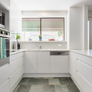 Design ideas for a contemporary u-shaped kitchen in Sydney with an undermount sink, flat-panel cabinets, white cabinets, white splashback, stainless steel appliances, a peninsula, blue floor and white benchtop.