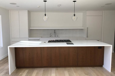 Inspiration for a large contemporary galley light wood floor eat-in kitchen remodel in New York with flat-panel cabinets, white cabinets, quartz countertops, white backsplash, paneled appliances and an island
