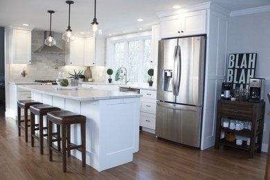 Inspiration for a mid-sized transitional l-shaped medium tone wood floor and brown floor eat-in kitchen remodel in Boston with a farmhouse sink, recessed-panel cabinets, white cabinets, quartzite countertops, gray backsplash, stone tile backsplash, stainless steel appliances and an island