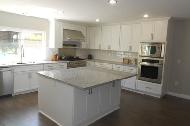 Example of a transitional u-shaped medium tone wood floor and brown floor eat-in kitchen design in San Diego with a single-bowl sink, shaker cabinets, white cabinets, quartz countertops, white backsplash, ceramic backsplash, stainless steel appliances and an island