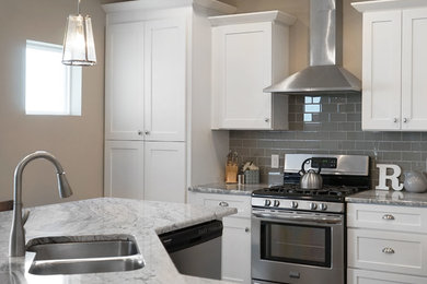 Example of a large trendy l-shaped medium tone wood floor eat-in kitchen design in Omaha with an undermount sink, shaker cabinets, white cabinets, granite countertops, white backsplash, ceramic backsplash, stainless steel appliances and an island