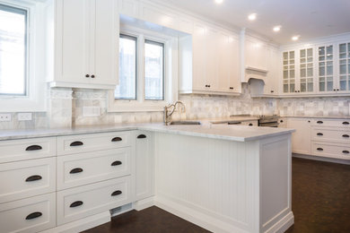 Example of a large transitional u-shaped dark wood floor and brown floor enclosed kitchen design in Toronto with an undermount sink, shaker cabinets, white cabinets, marble countertops, white backsplash, stone tile backsplash, stainless steel appliances and a peninsula