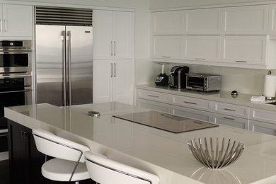 Example of a mid-sized minimalist l-shaped dark wood floor eat-in kitchen design in Miami with an undermount sink, shaker cabinets, white cabinets, white backsplash, glass tile backsplash, stainless steel appliances, an island and solid surface countertops