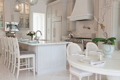 Cette photo montre une cuisine américaine chic en L avec un placard avec porte à panneau surélevé, des portes de placard blanches, plan de travail en marbre, une crédence blanche et îlot.