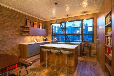 Eat-in kitchen - large industrial galley light wood floor and brown floor eat-in kitchen idea in New York with a single-bowl sink, flat-panel cabinets, gray cabinets, granite countertops, brick backsplash and an island