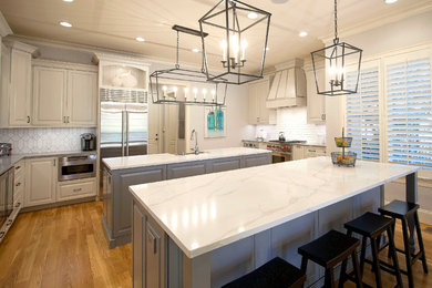 Inspiration for a large transitional l-shaped light wood floor enclosed kitchen remodel in Charlotte with a farmhouse sink, glass-front cabinets, white cabinets, granite countertops, gray backsplash, porcelain backsplash, stainless steel appliances and two islands