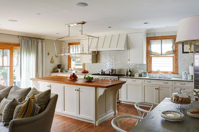 Klassisk inredning av ett stort kök, med en nedsänkt diskho, släta luckor, vita skåp, träbänkskiva, vitt stänkskydd, rostfria vitvaror, mellanmörkt trägolv och en köksö