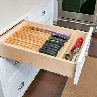 Cette photo montre une cuisine américaine chic en U de taille moyenne avec un évier de ferme, un placard à porte shaker, des portes de placard blanches, un plan de travail en surface solide, une crédence multicolore, une crédence en mosaïque, un électroménager en acier inoxydable, un sol en contreplaqué et un îlot central.