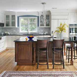 Example of a large transitional l-shaped light wood floor and brown floor enclosed kitchen design in New York with raised-panel cabinets, white cabinets, stainless steel appliances, an undermount sink, granite countertops, gray backsplash, marble backsplash and an island