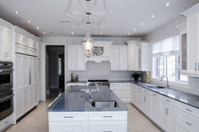 Example of a large trendy u-shaped porcelain tile eat-in kitchen design in New York with an undermount sink, recessed-panel cabinets, white cabinets, granite countertops, white backsplash, ceramic backsplash, paneled appliances and an island