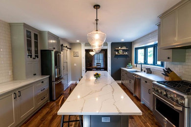 Large transitional u-shaped dark wood floor and brown floor eat-in kitchen photo in Milwaukee with a farmhouse sink, beaded inset cabinets, gray cabinets, quartz countertops, white backsplash, subway tile backsplash, stainless steel appliances and an island