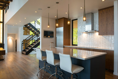 Eat-in kitchen - mid-sized modern galley medium tone wood floor and brown floor eat-in kitchen idea in Minneapolis with an undermount sink, flat-panel cabinets, quartz countertops, white backsplash, subway tile backsplash, stainless steel appliances, an island and dark wood cabinets