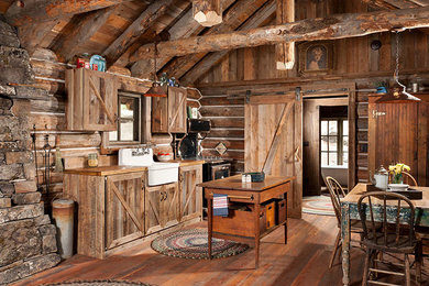 Inspiration for a mid-sized rustic single-wall medium tone wood floor open concept kitchen remodel in Jackson with a farmhouse sink, shaker cabinets, distressed cabinets, wood countertops, brown backsplash, wood backsplash, black appliances and an island