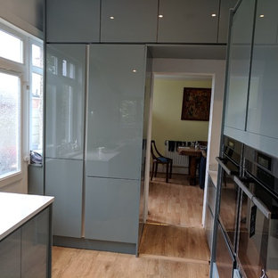 Foto di una cucina ad U moderna chiusa e di medie dimensioni con lavello sottopiano, ante lisce, ante turchesi, top in quarzite, paraspruzzi bianco, paraspruzzi in lastra di pietra, elettrodomestici neri, pavimento in vinile, nessuna isola, pavimento marrone e top bianco