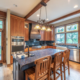Design ideas for a mid-sized country u-shaped eat-in kitchen in Milwaukee with a farmhouse sink, recessed-panel cabinets, medium wood cabinets, recycled glass benchtops, blue splashback, terra-cotta splashback, stainless steel appliances, medium hardwood floors, with island, yellow floor and blue benchtop.