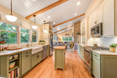 Bild på ett stort lantligt kök, med en rustik diskho, luckor med infälld panel, gröna skåp, bänkskiva i kvarts, vitt stänkskydd, stänkskydd i tunnelbanekakel, rostfria vitvaror, ljust trägolv och en köksö