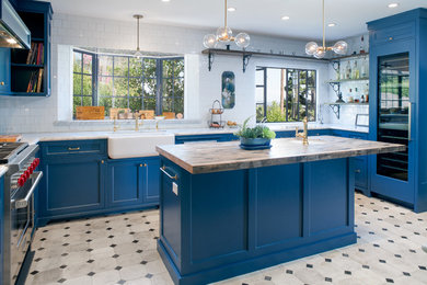 Large tuscan u-shaped concrete floor and multicolored floor kitchen photo in Los Angeles with a farmhouse sink, recessed-panel cabinets, blue cabinets, marble countertops, white backsplash, subway tile backsplash, paneled appliances and an island