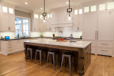 Mid-sized farmhouse l-shaped light wood floor and brown floor eat-in kitchen photo in DC Metro with an undermount sink, recessed-panel cabinets, white cabinets, white backsplash, subway tile backsplash, paneled appliances, an island and black countertops