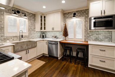 Example of a mid-sized classic galley medium tone wood floor and brown floor enclosed kitchen design in Columbus with a farmhouse sink, shaker cabinets, white cabinets, quartz countertops, multicolored backsplash, ceramic backsplash, stainless steel appliances, white countertops and an island