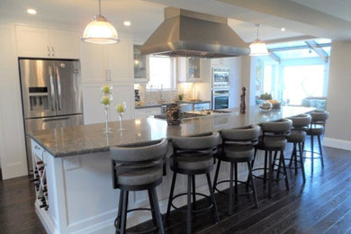 Eat-in kitchen - large transitional single-wall dark wood floor and brown floor eat-in kitchen idea in Toronto with a farmhouse sink, recessed-panel cabinets, white cabinets, granite countertops, beige backsplash, porcelain backsplash, stainless steel appliances and an island