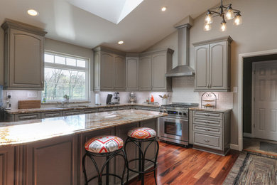 Inspiration for a large traditional u-shaped open plan kitchen in St Louis with a double-bowl sink, raised-panel cabinets, grey cabinets, granite worktops, white splashback, metro tiled splashback, stainless steel appliances, dark hardwood flooring and an island.