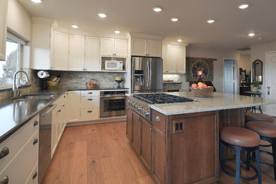 Example of a mid-sized transitional l-shaped medium tone wood floor and brown floor eat-in kitchen design in Portland with an undermount sink, recessed-panel cabinets, white cabinets, quartz countertops, beige backsplash, stone tile backsplash, stainless steel appliances and an island