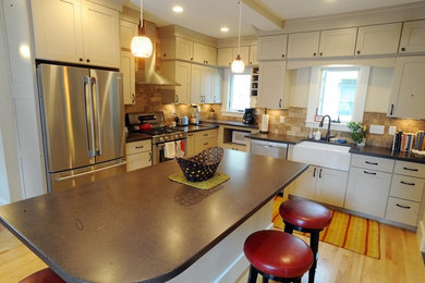 Example of a mid-sized classic light wood floor kitchen design in Burlington with shaker cabinets, beige cabinets, solid surface countertops, beige backsplash, stone tile backsplash, stainless steel appliances and an island
