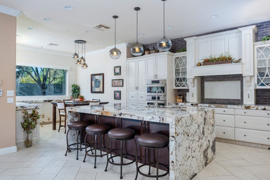 Example of a transitional light wood floor and white floor eat-in kitchen design in Phoenix with raised-panel cabinets, white cabinets, gray backsplash, brick backsplash, stainless steel appliances, an island and multicolored countertops