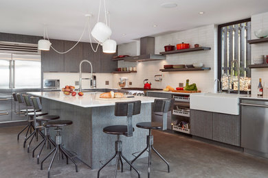 Example of a 1950s l-shaped concrete floor and gray floor kitchen design in San Francisco with a farmhouse sink, flat-panel cabinets, gray cabinets, white backsplash, stainless steel appliances, an island and white countertops