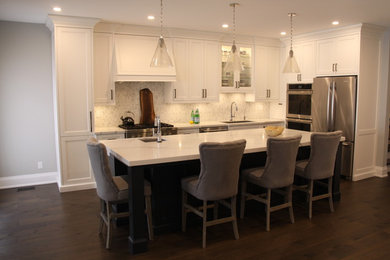 Mid-sized transitional l-shaped dark wood floor and brown floor kitchen photo in Toronto with an undermount sink, recessed-panel cabinets, white cabinets, quartzite countertops, white backsplash, marble backsplash, stainless steel appliances, an island and white countertops