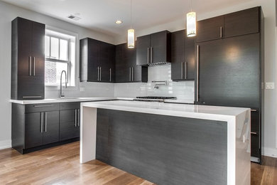 Eat-in kitchen - mid-sized contemporary galley light wood floor eat-in kitchen idea in Chicago with a drop-in sink, flat-panel cabinets, black cabinets, solid surface countertops, white backsplash, subway tile backsplash, stainless steel appliances and an island