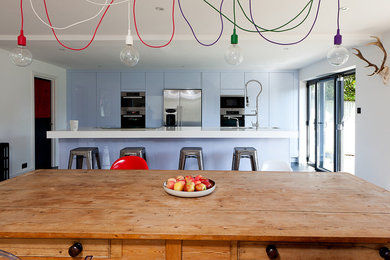 Стильный дизайн: параллельная кухня в современном стиле с обеденным столом, плоскими фасадами, синими фасадами и техникой из нержавеющей стали - последний тренд