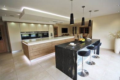 Inspiration for a large contemporary kitchen in Essex with flat-panel cabinets, black appliances, porcelain flooring and multiple islands.