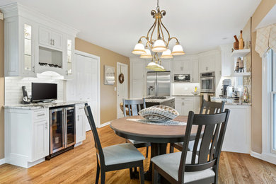 Mid-sized trendy l-shaped light wood floor and brown floor eat-in kitchen photo in Chicago with a drop-in sink, shaker cabinets, white cabinets, granite countertops, white backsplash, ceramic backsplash, stainless steel appliances, an island and multicolored countertops